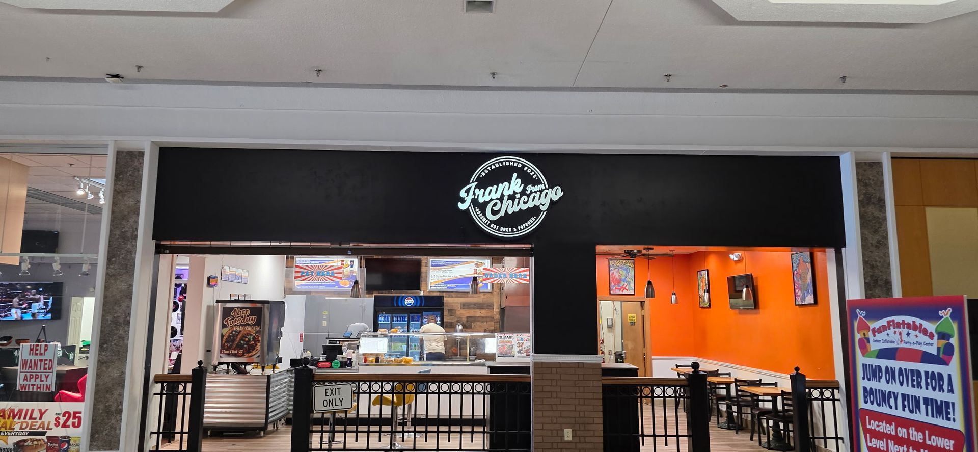 Mall food stall with black sign, orange wall, and empty dining tables in front