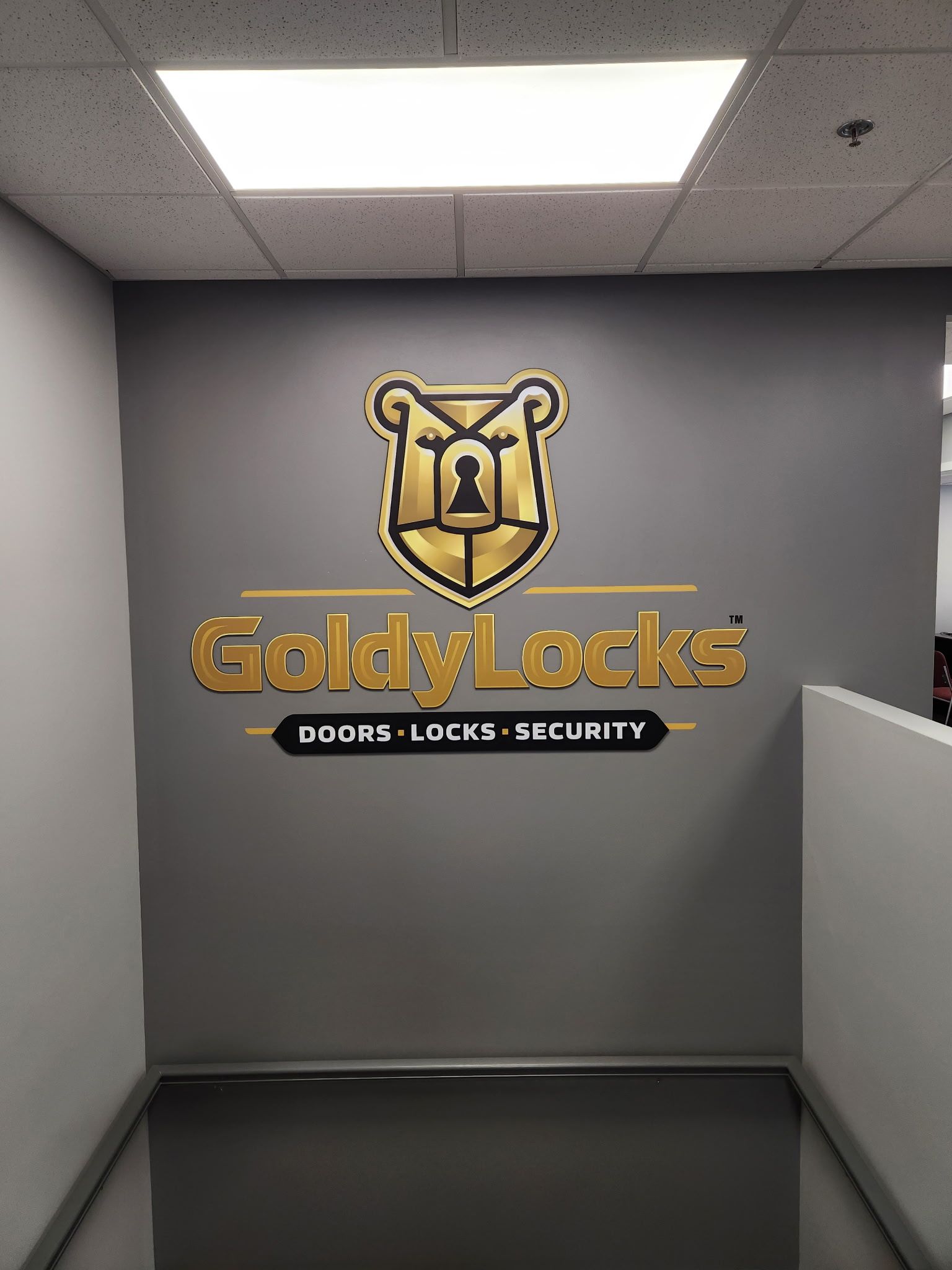 GoldyLocks logo on a gray wall in an office hallway, with a gold bear emblem and the words “Doors · Locks · Security”