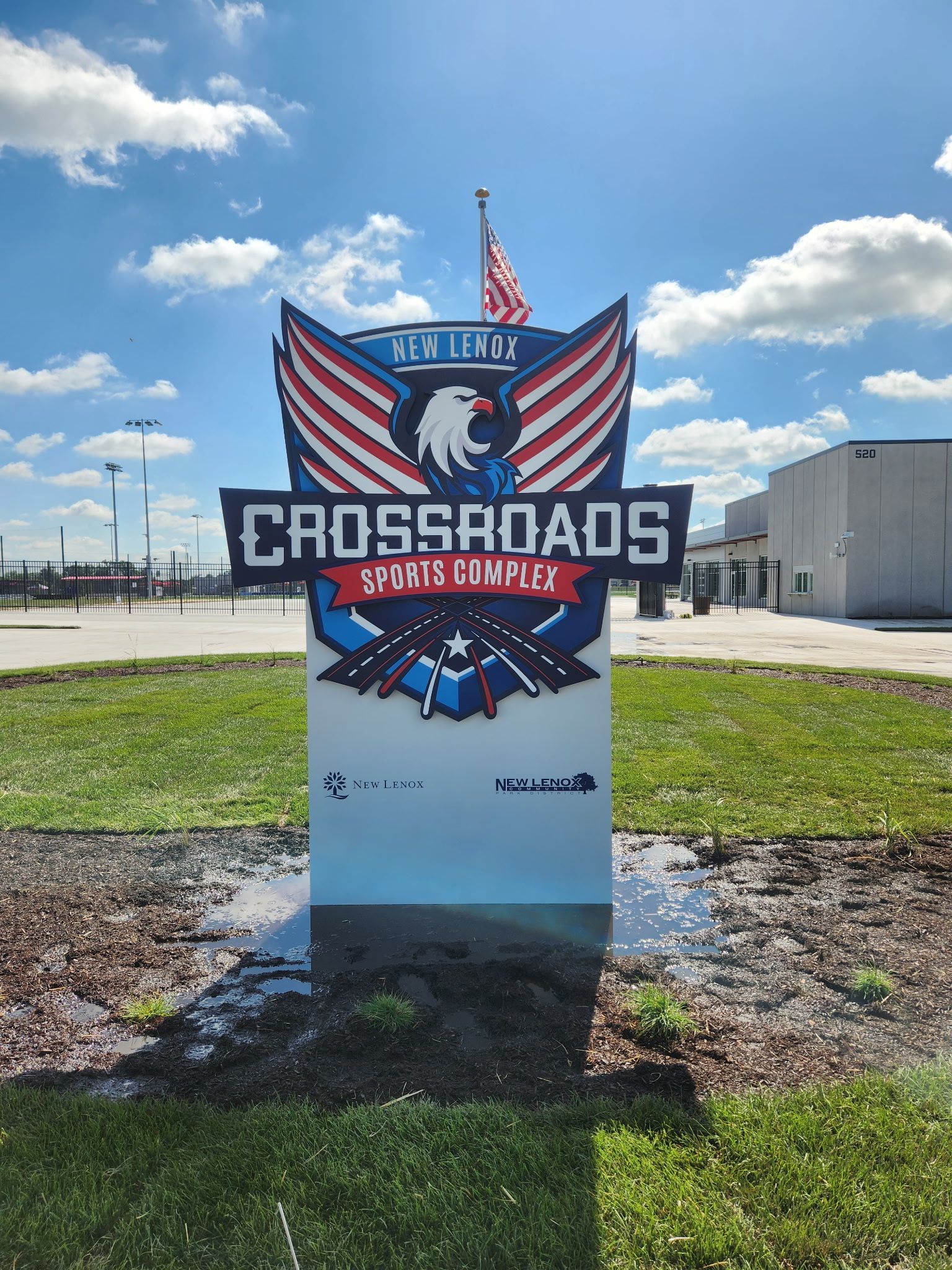 Crossroads sports complex sign with red and blue eagle wings under a sunny blue sky.