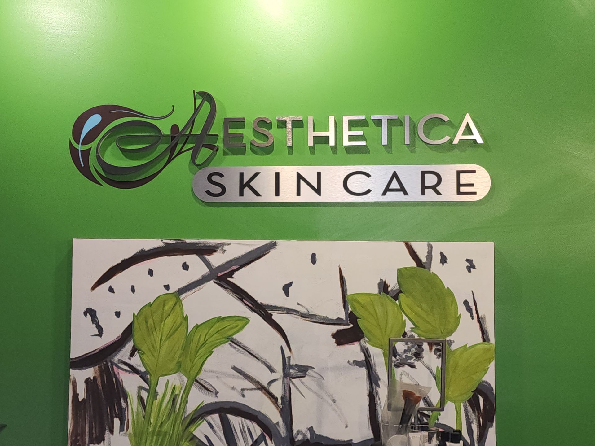 A green sign reading “Aesthetica Skin Care” above a plant-themed wall display.