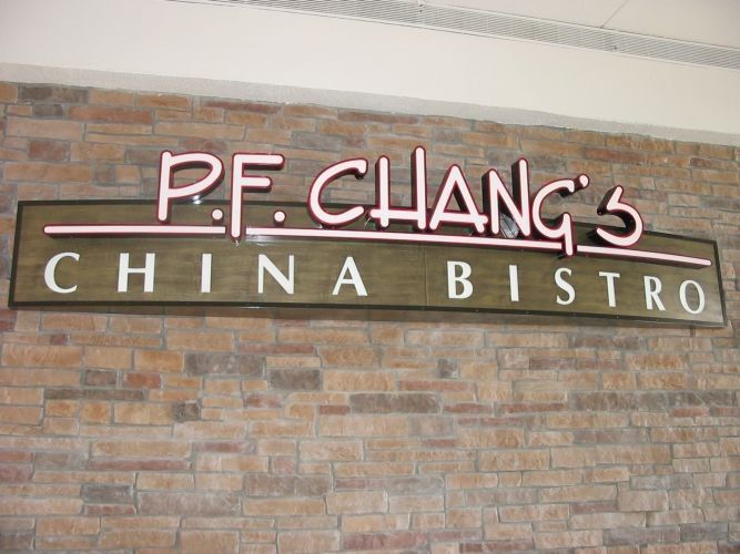 P.F. Chang's China Bistro sign on a brick wall. The sign has pink neon and a wooden frame.