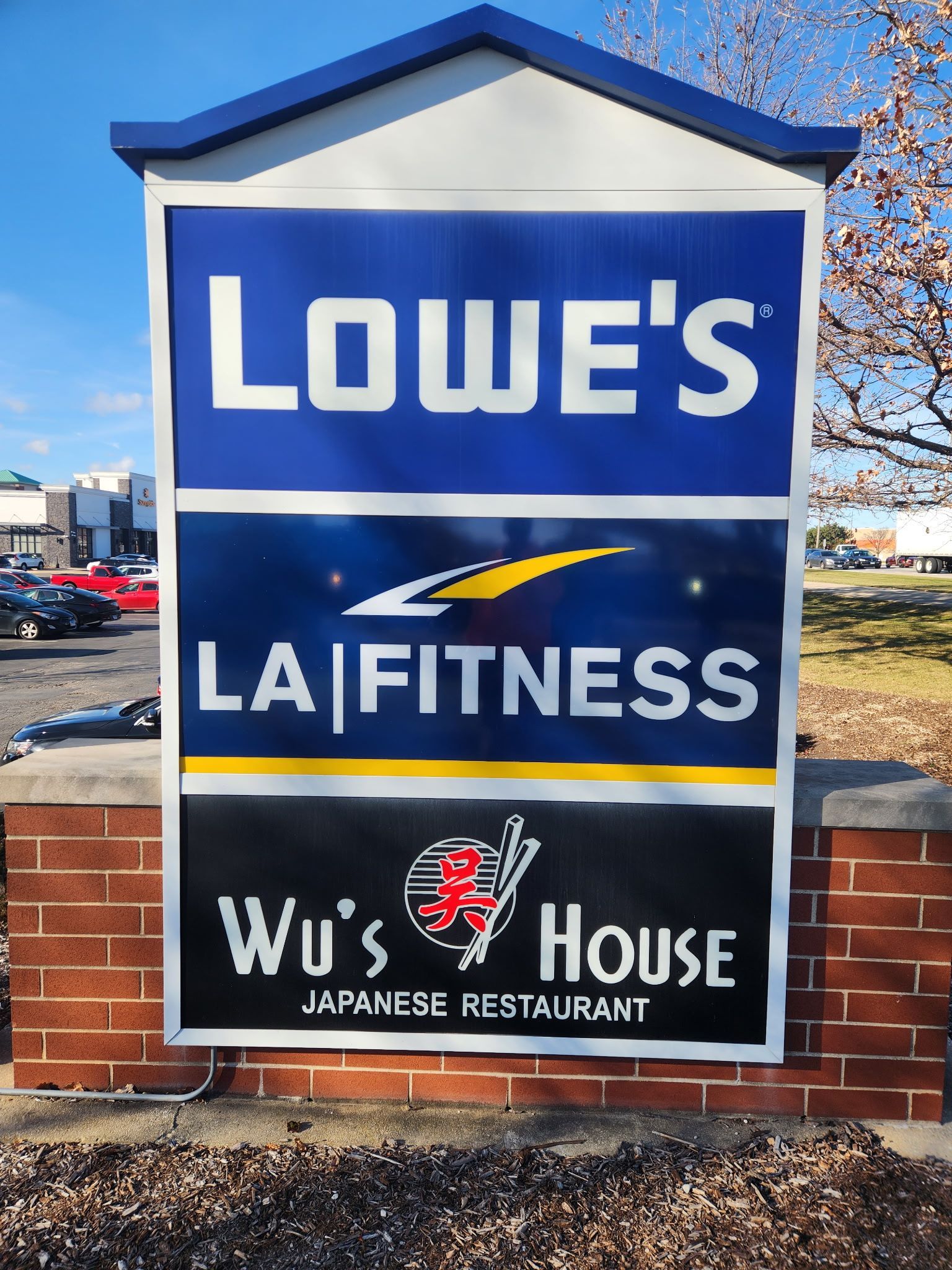 Lowe's, LA Fitness and Wu's House signs on a roadside business monument under a blue sky