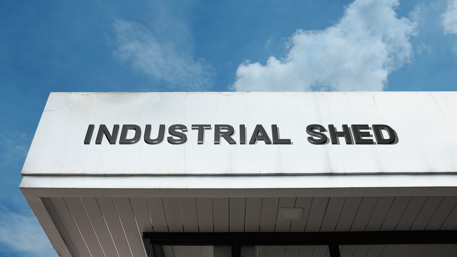 Building facade with “INDUSTRIAL SHED” sign against a blue sky with clouds.