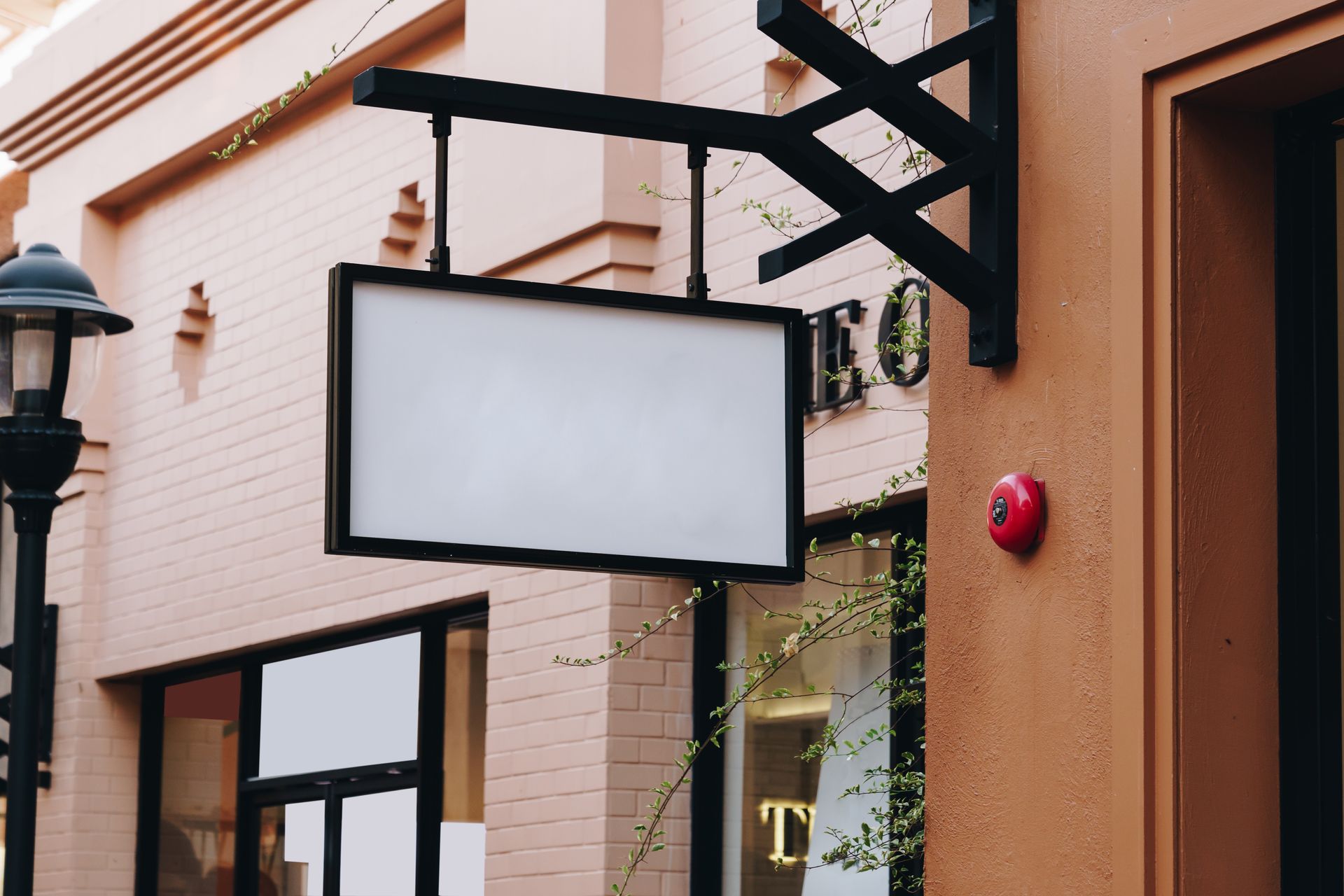 A blank rectangular blade sign on a black mounting bracket extending from a brick storefront facade