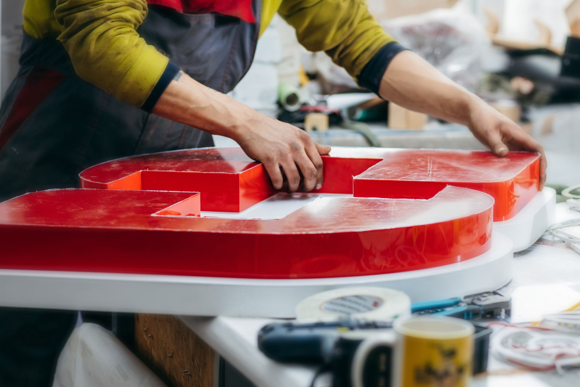 Person assembling a large red sign letter on a workshop table. Person assembling a large red sign letter on a workshop table.