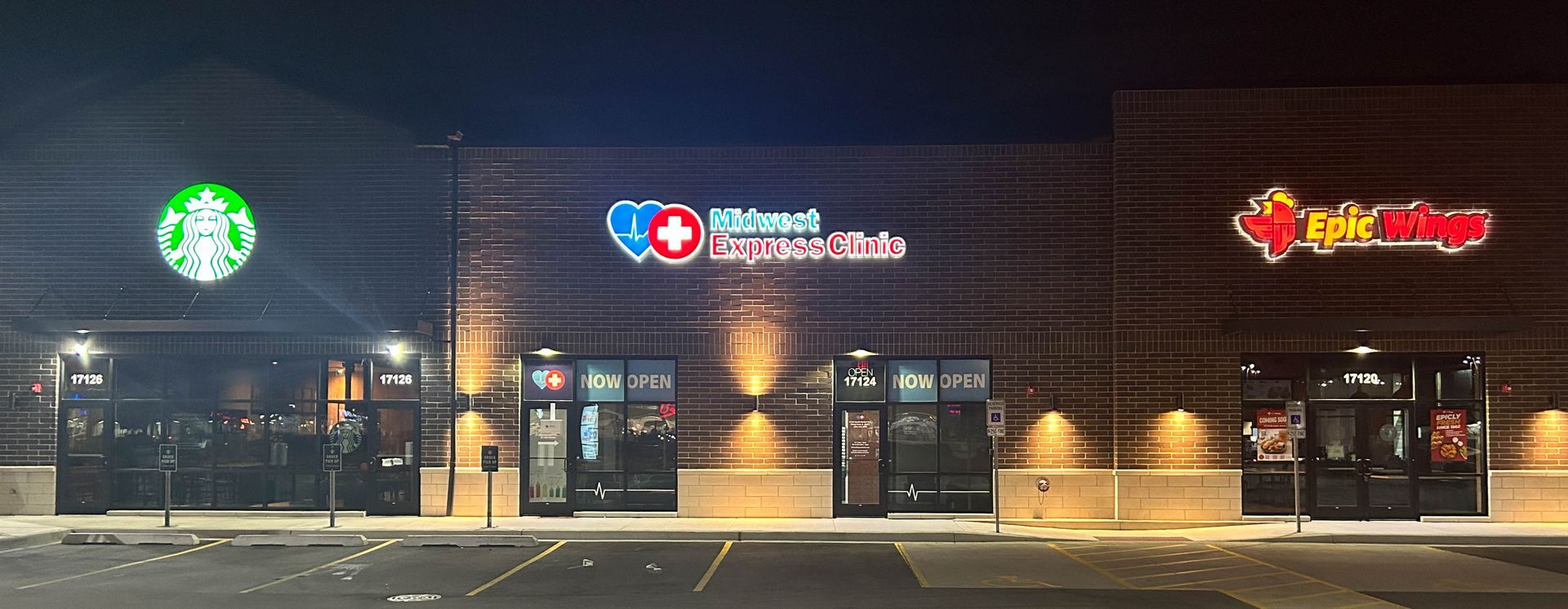 Nighttime storefronts in a strip mall, with a green circular sign, a pharmacy, and a Thai restaurant.