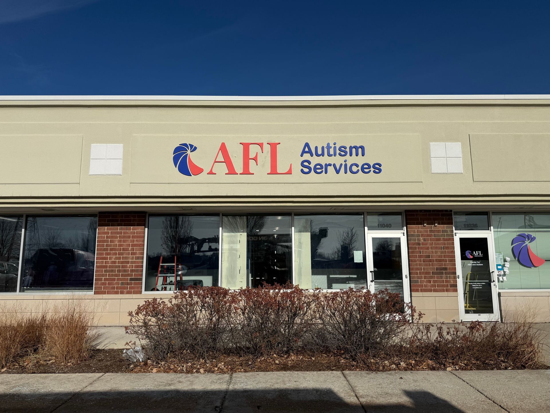 AFL Autism Services storefront with beige facade, red and blue sign, and windows above bushes