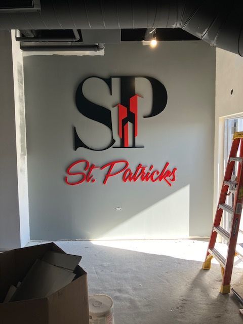 Interior wall with large SP logo and red “St. Patrick’s” lettering, in a room under renovation