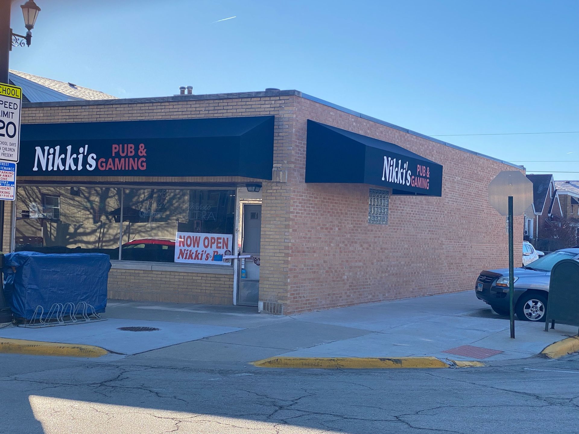 Mikk’s Pub & Gaming on a brick corner building with blue awnings and a dumpster outside
