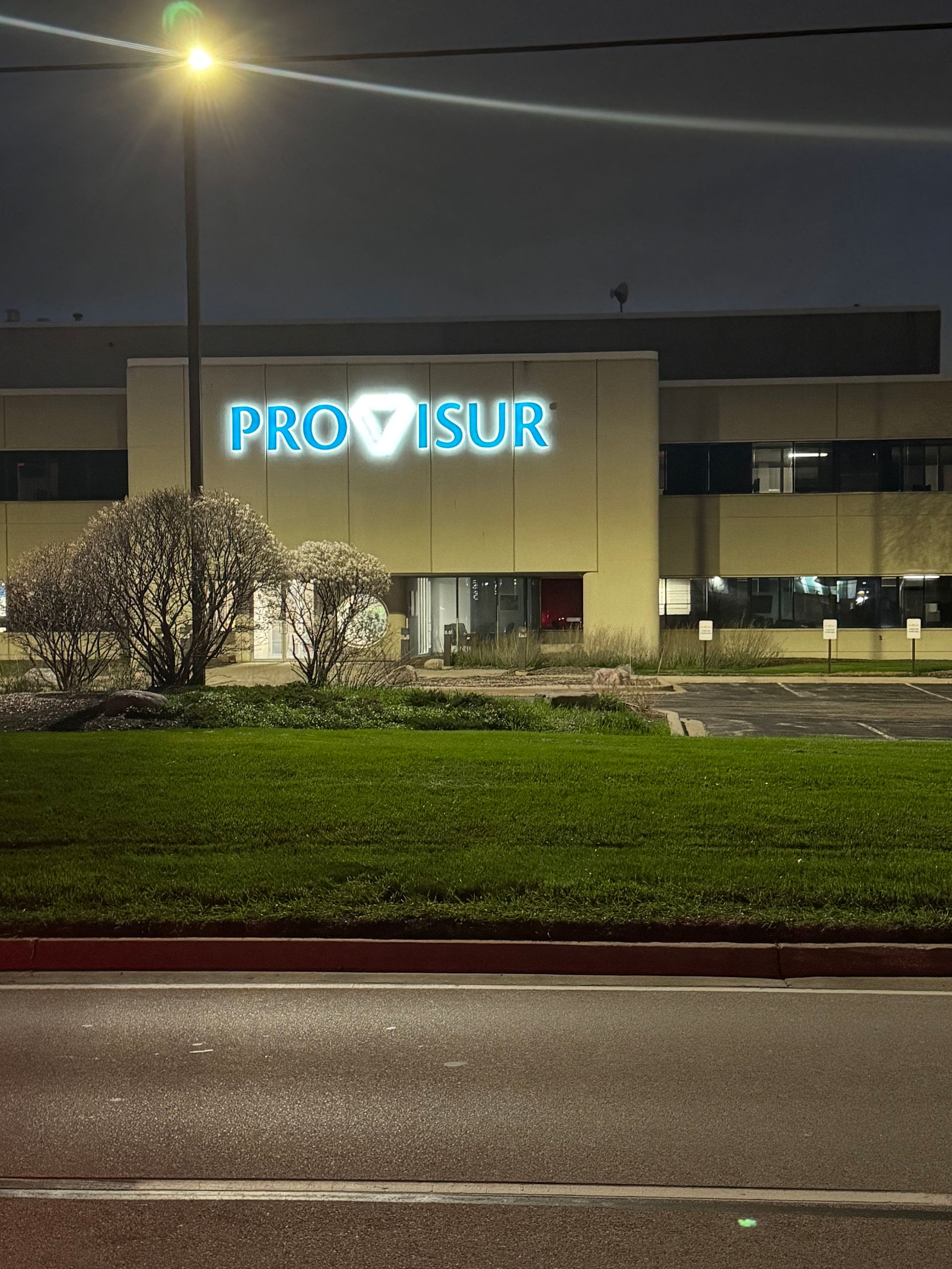 Night photo of a PROVISUR office building with a glowing sign, streetlight, and grassy foreground.