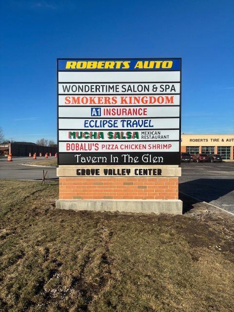 Roadside business sign for Roberts Auto, listing shops in a tan-and-blue plaza under a clear sky