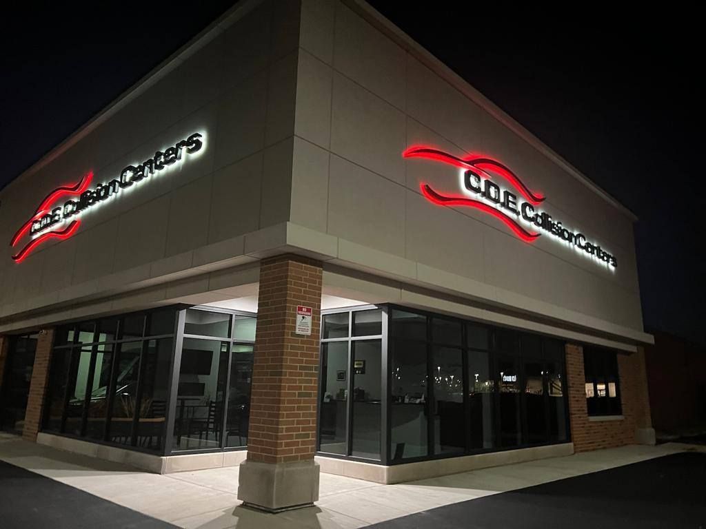 Corner view of a lit H-E-B store at night with glass windows and red signs
