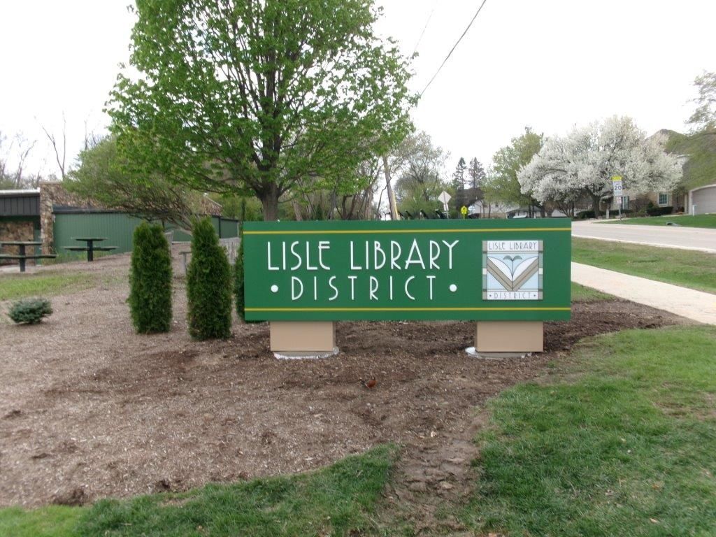 Lisle Library District sign in green near trees and a landscaped sidewalk