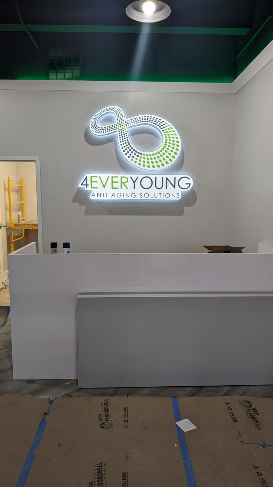Modern reception desk in a white room with a glowing “EVERYOUNG” wall sign