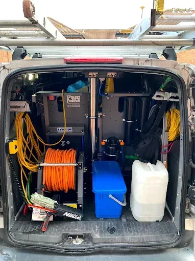 Open back of a van, filled with window washing equipment and supplies.  Orange and yellow hoses, tanks, and cleaning tools are visible.
