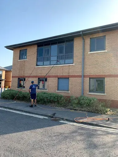 A person washing windows on a two-story brick building with a long-handled brush.
