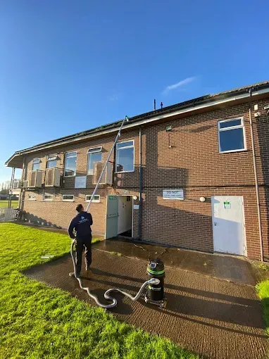 Man cleaning building windows with a long pole and vacuum, against a blue sky.