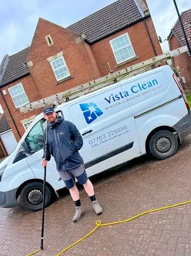 Man stands next to a white Vista Clean van, holding a pole. Brown brick house in background.