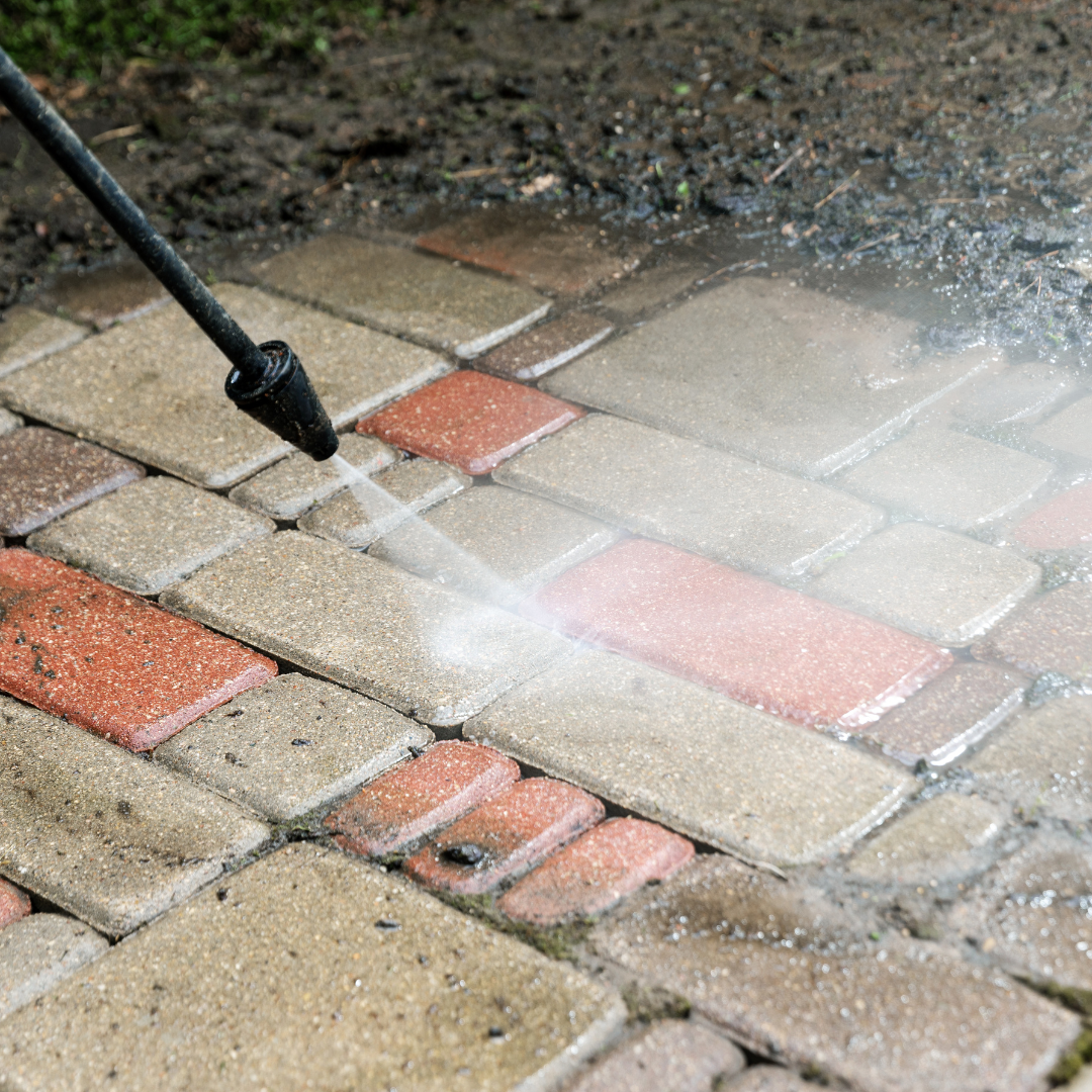 Pressure washer cleaning red and tan brick pavers.