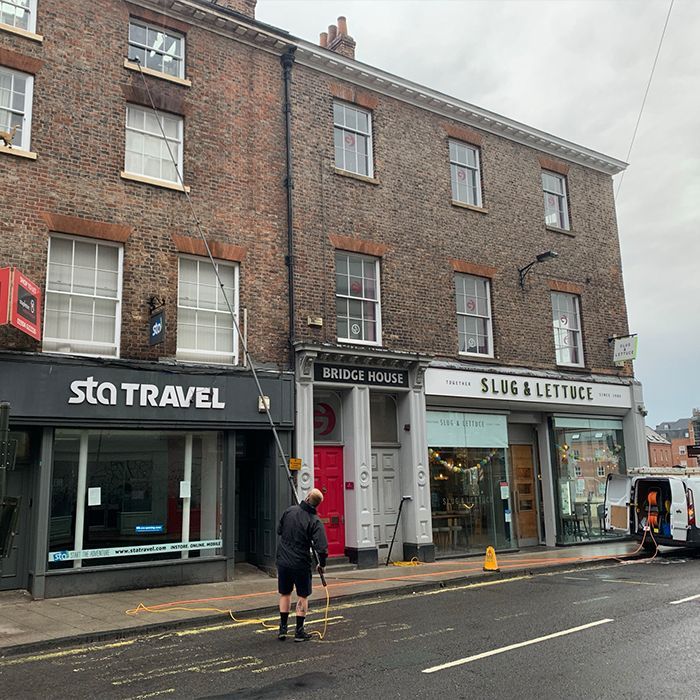 Man washing windows on brick building with shopfronts: STA Travel, Bridge House, and Slug & Lettuce.
