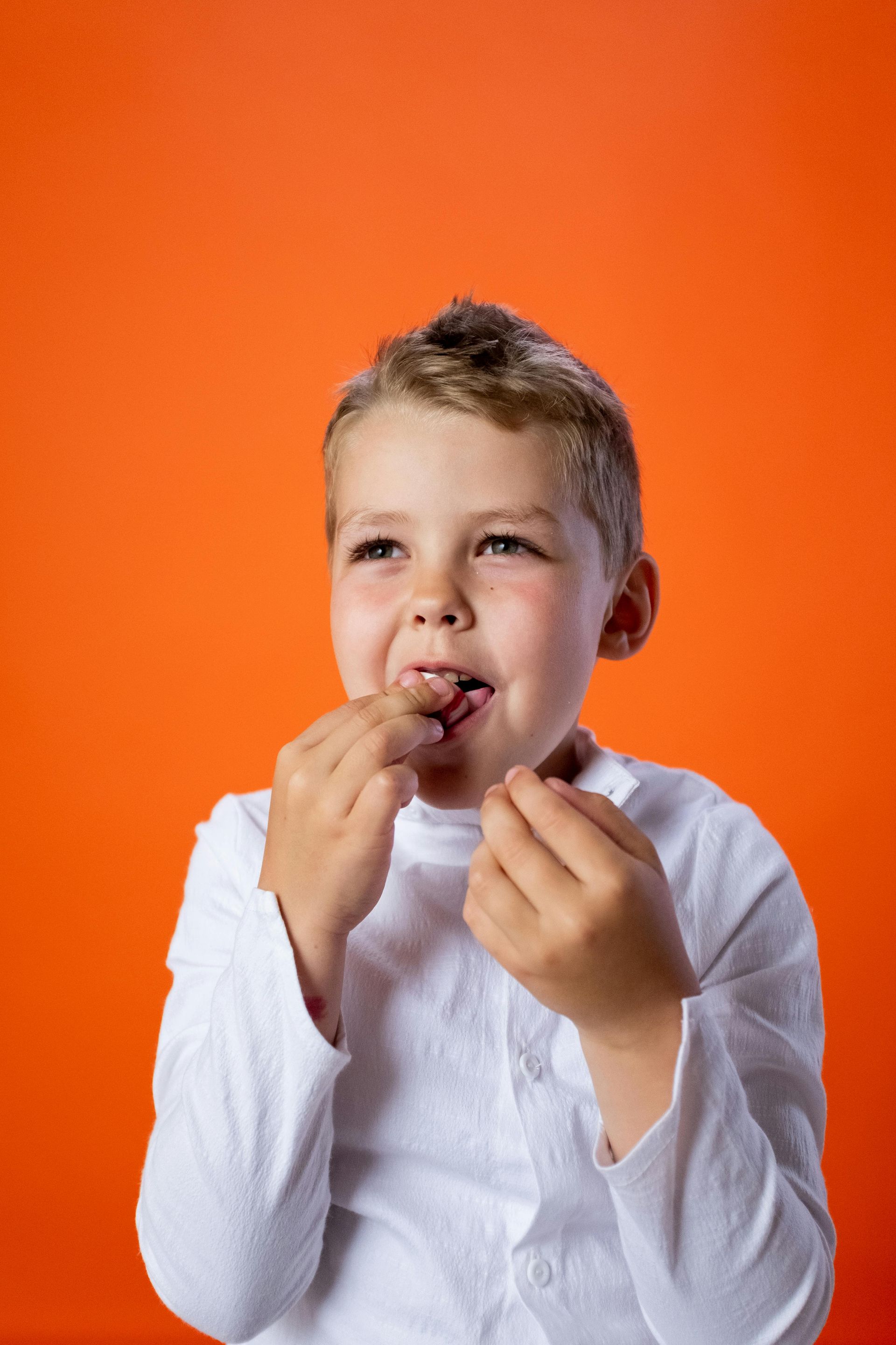 Child in a white shirt eating candy against an orange background
