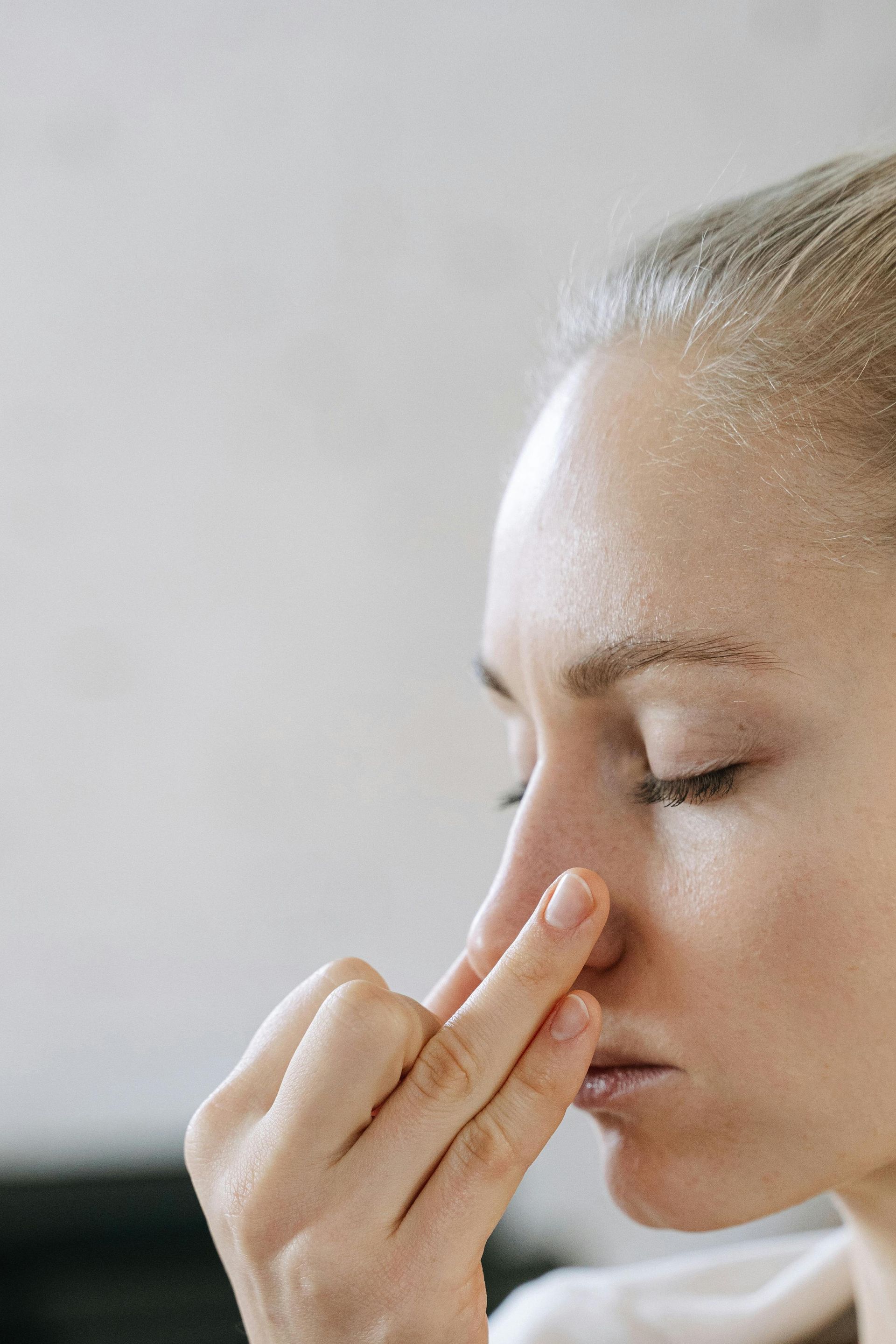 Woman pinching her nose with eyes closed against a plain light background