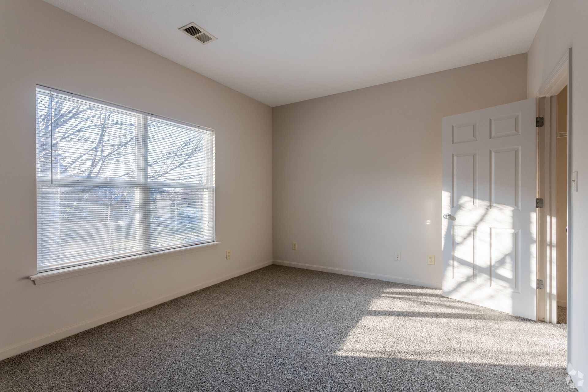An empty bedroom with a window and blinds.