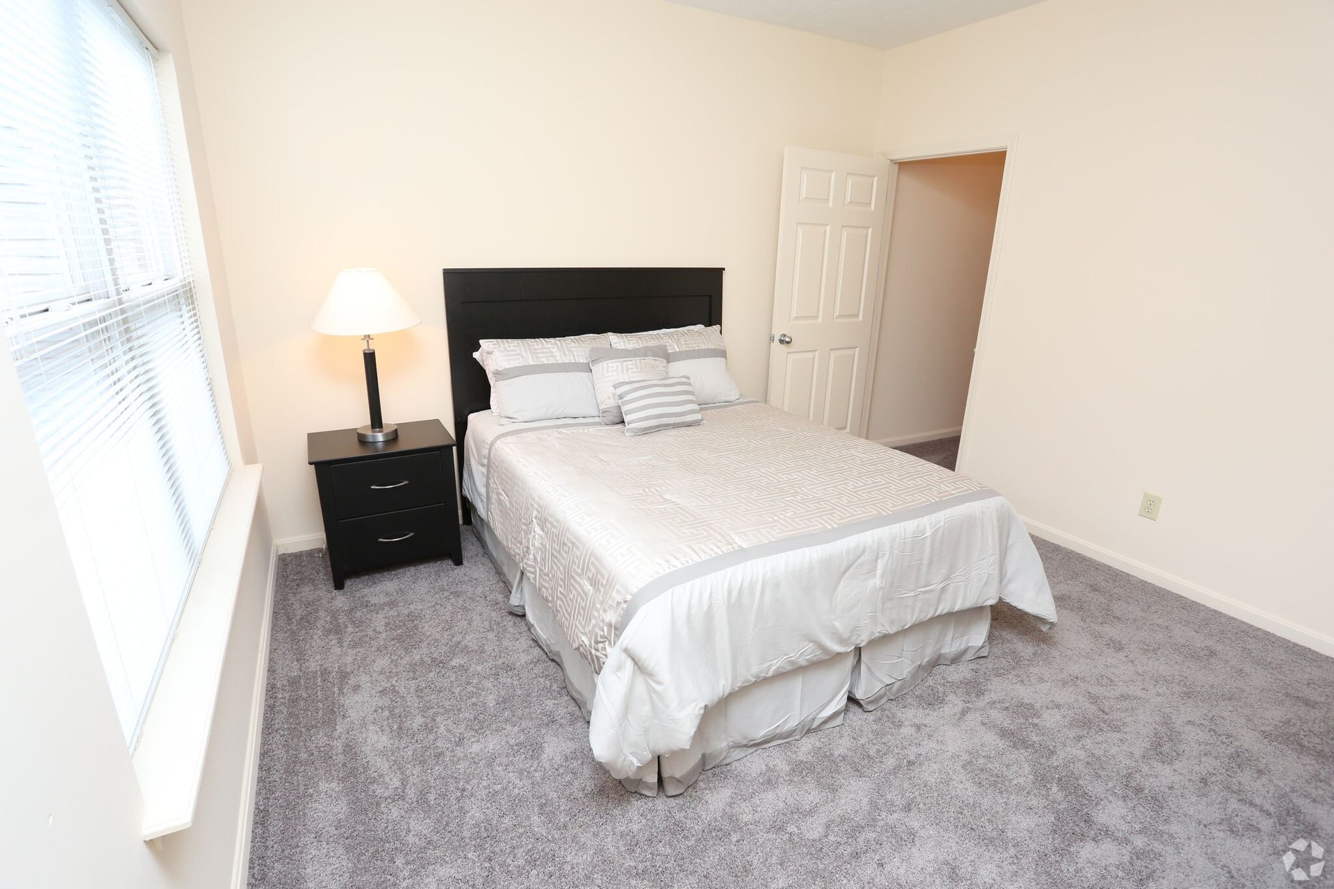 A bedroom with a bed , nightstand , lamp and window.