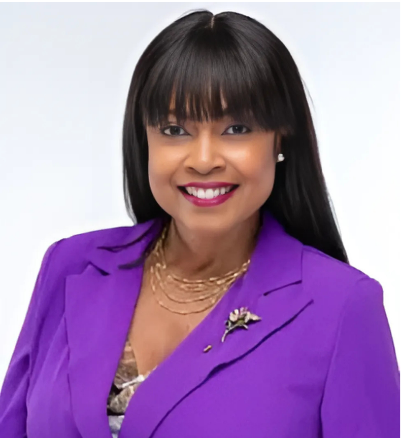 Woman with dark hair and bangs wearing a purple blazer, smiling at the camera.