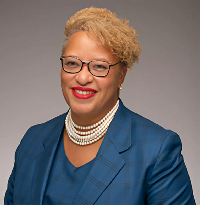 Woman with glasses, blonde hair, red lipstick, and pearl necklace, wearing a blue blazer.