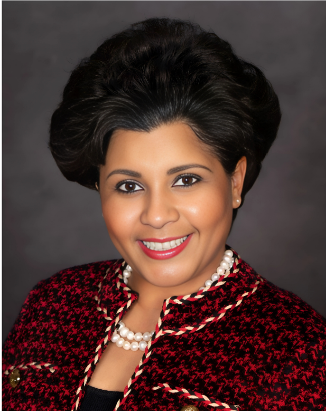 Smiling woman in a red jacket and pearl necklace. Dark hair, medium skin tone, against a neutral background.