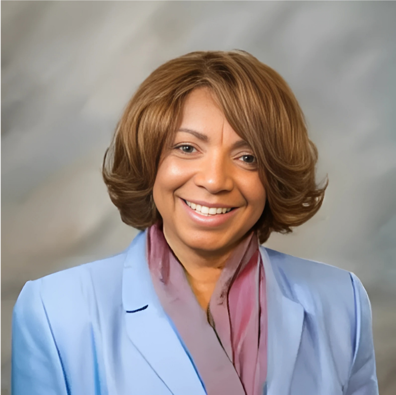 Woman with short brown hair, smiling in a light blue blazer with a pink scarf.