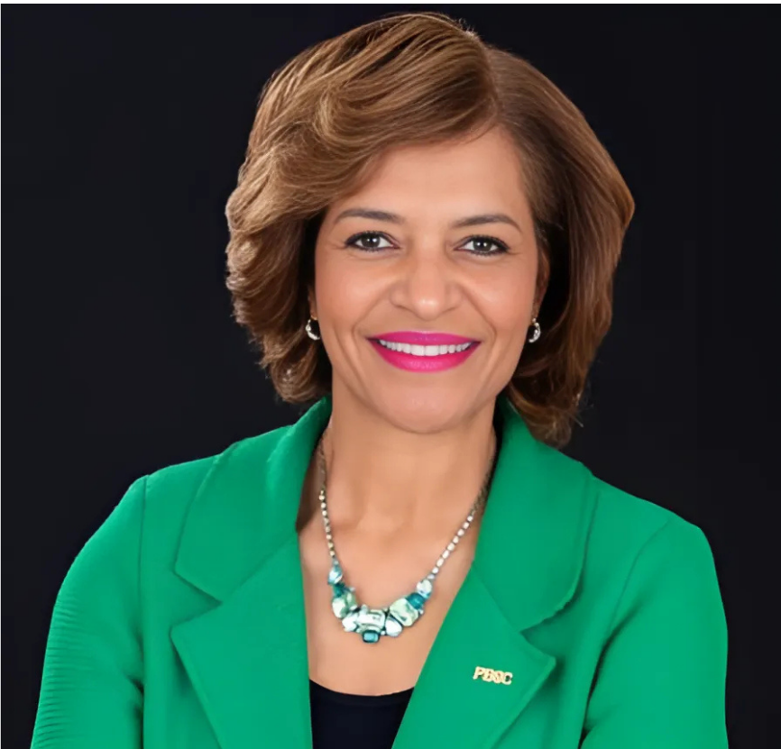 Woman with brown hair, green jacket, smiling at the camera, against a black background.