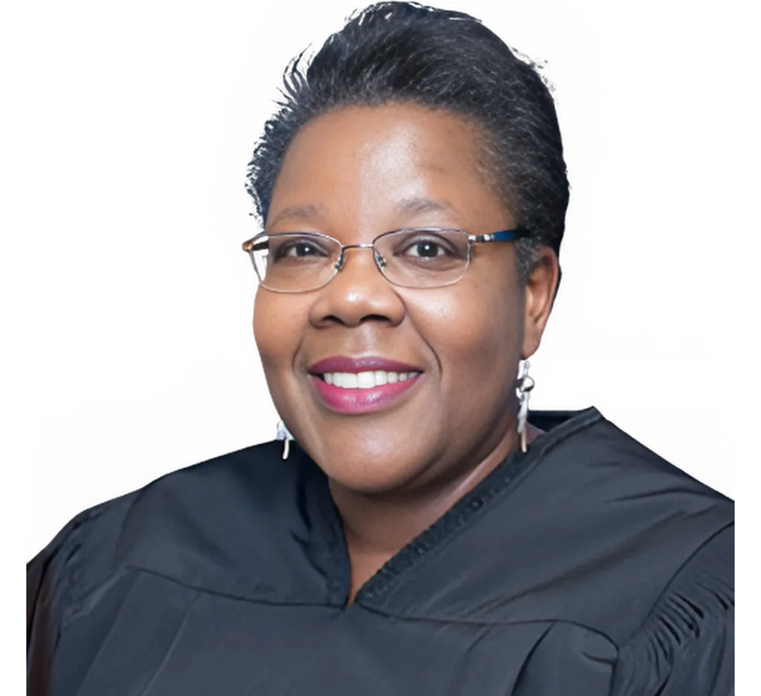 Judge smiling, wearing glasses and black robe.