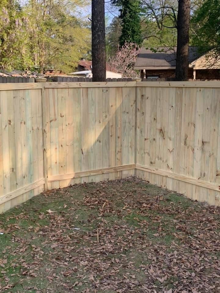 A new light-colored wooden privacy fence forms an L-shaped corner in a grassy yard covered with fallen leaves.