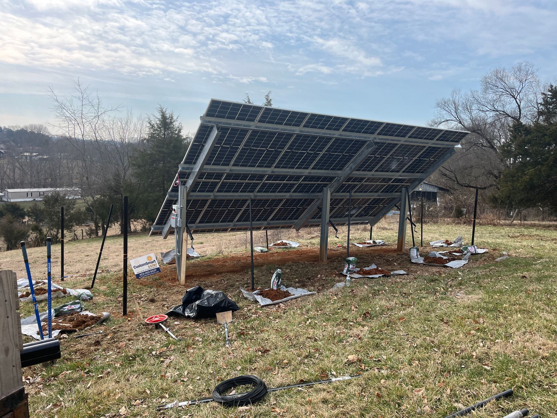 A ground-mounted solar panel array under construction in an open, grassy field during the daytime.