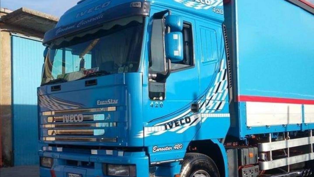 Camion Iveco Eurocargo 40 blu con dettagli grafici bianchi, parcheggiato vicino a un edificio.