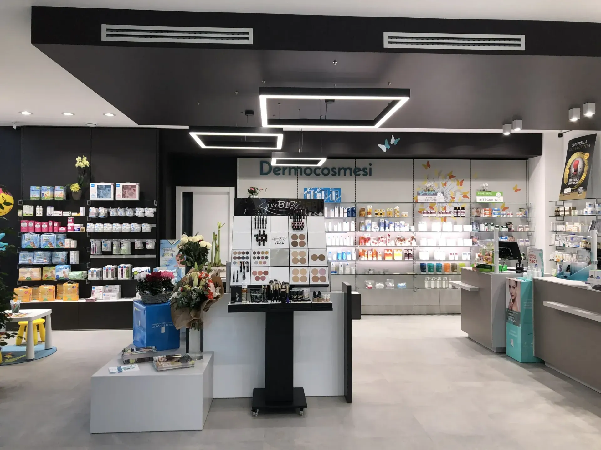 Interno luminoso di un negozio di cosmetici con scaffali pieni di prodotti per la cura della pelle e un tavolo espositivo centrale.