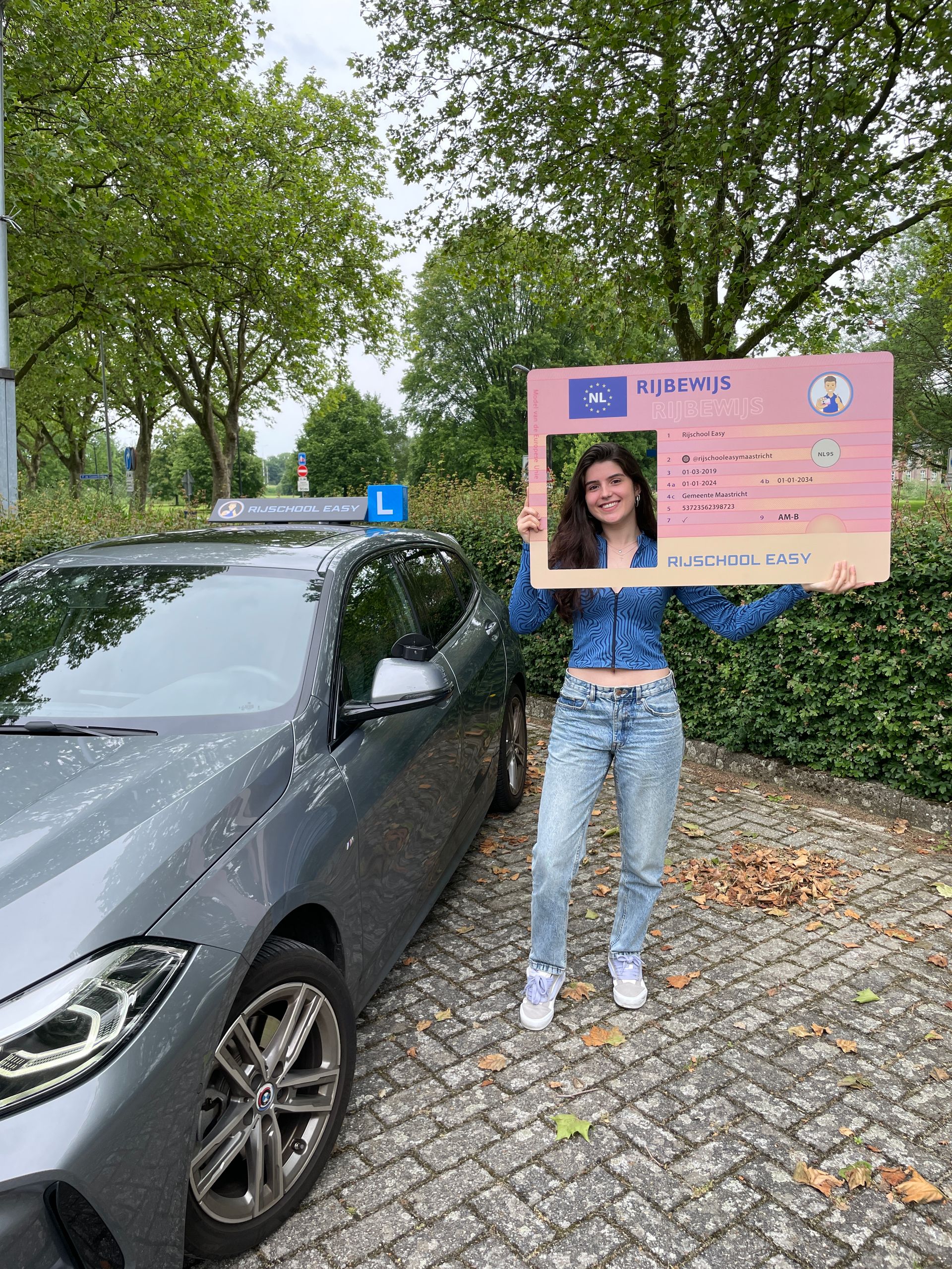 Een geslaagde leerling houdt een bord vast voor de lesauto van rijschool easy.