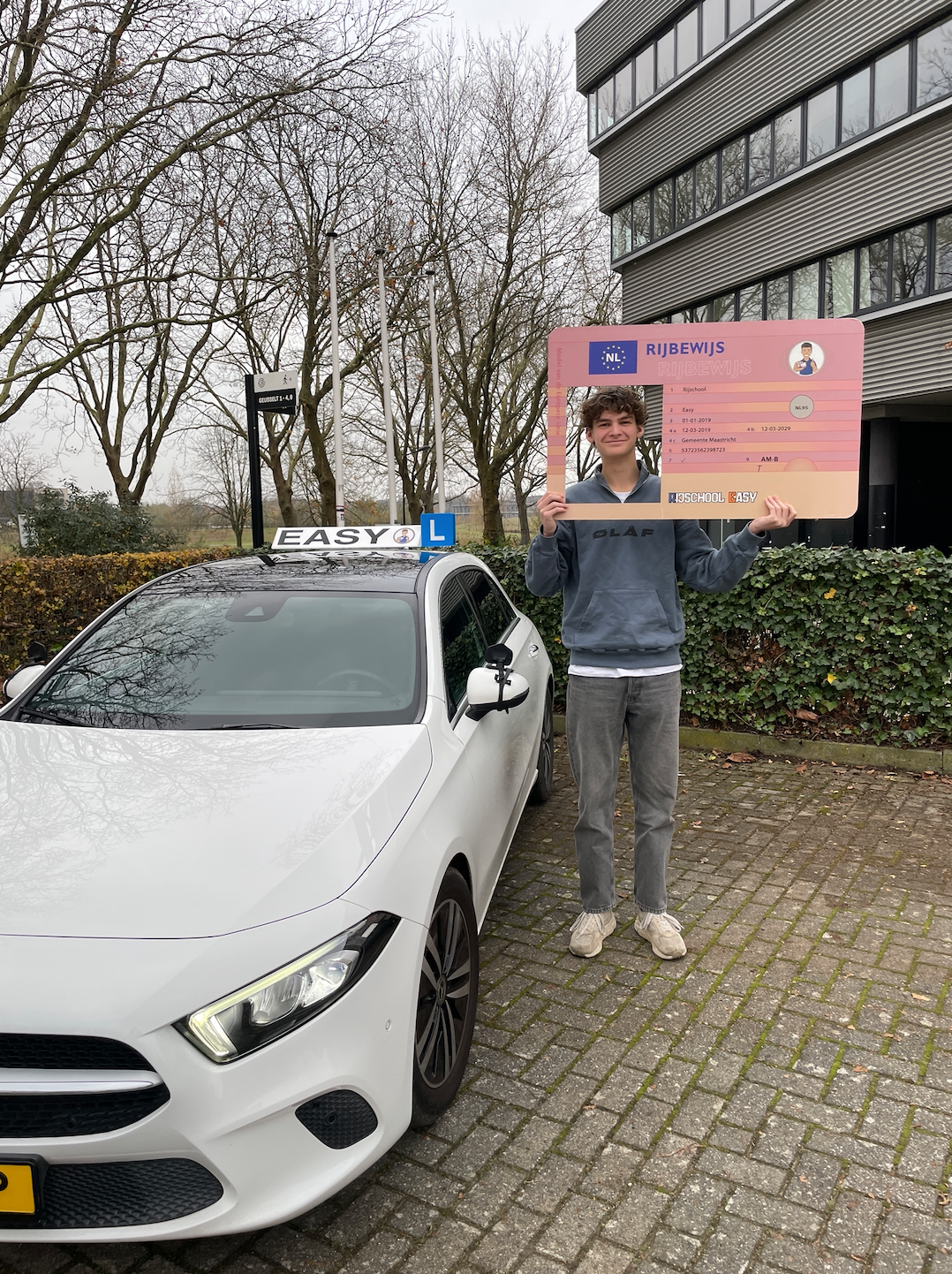 Een geslaagde kandidaat houdt een rijbewijs vast voor een de lesauto van rijschool easy.