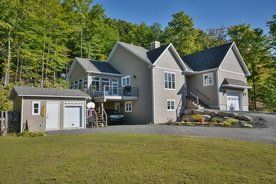 Une grande maison avec un garage et un hangar devant entourée d'arbres.