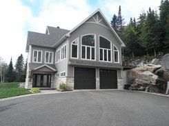 Une grande maison avec deux portes de garage est située au sommet d'une colline.