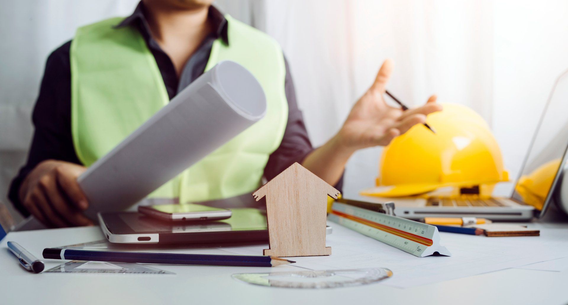 Un ouvrier du bâtiment est assis à un bureau avec un ordinateur portable et un plan.