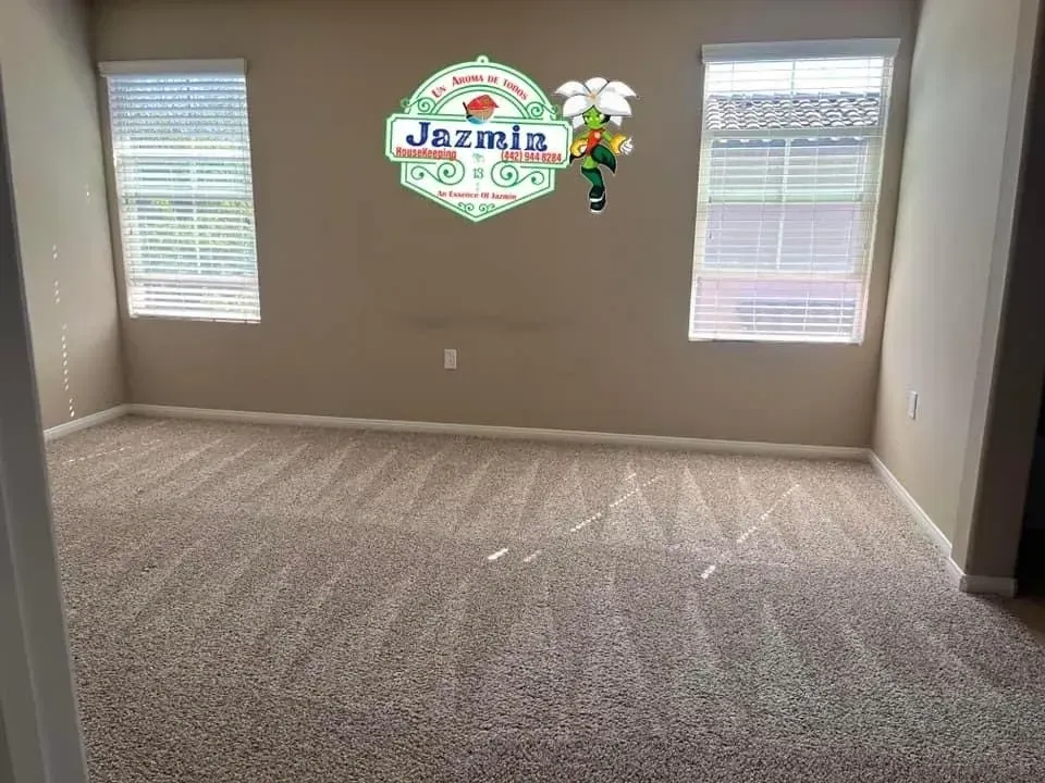 Empty beige room with carpet, two windows, and a Jesmir logo on the wall.