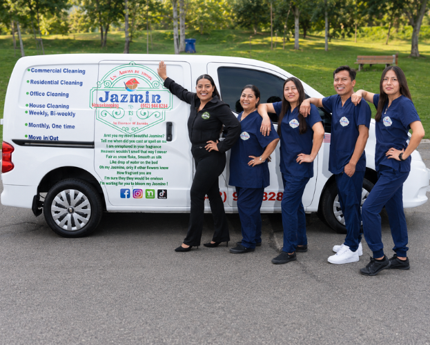 Five people stand beside a white service van with a Jazmine Cleaning logo and blue uniforms.