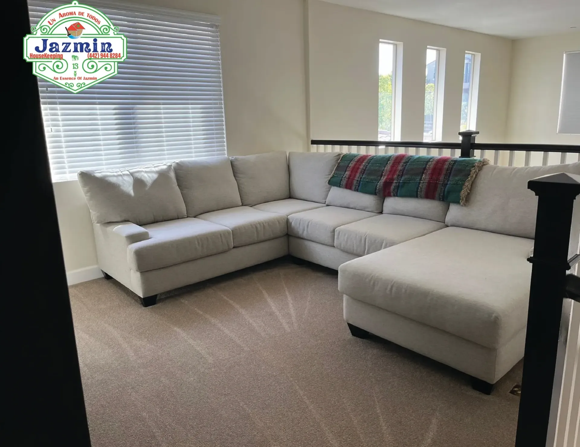 Bright living room with a light gray sectional sofa, carpeted floor, and windows with blinds and narrow skylights.