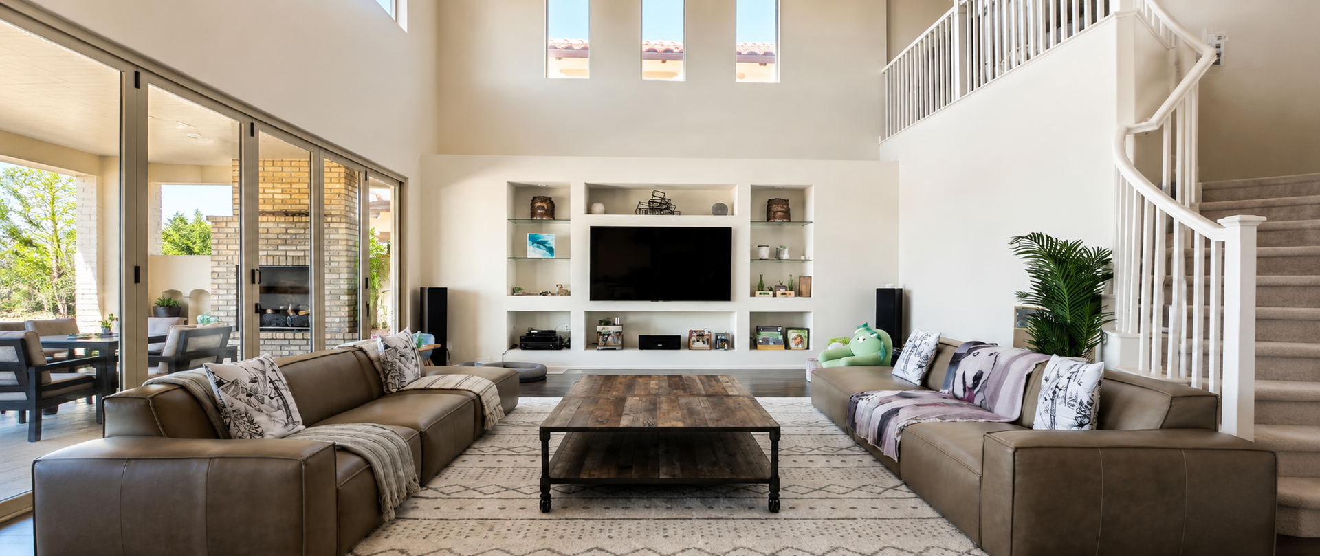Bright living room with beige sofas, a fireplace TV wall, tall windows, and a coffee table