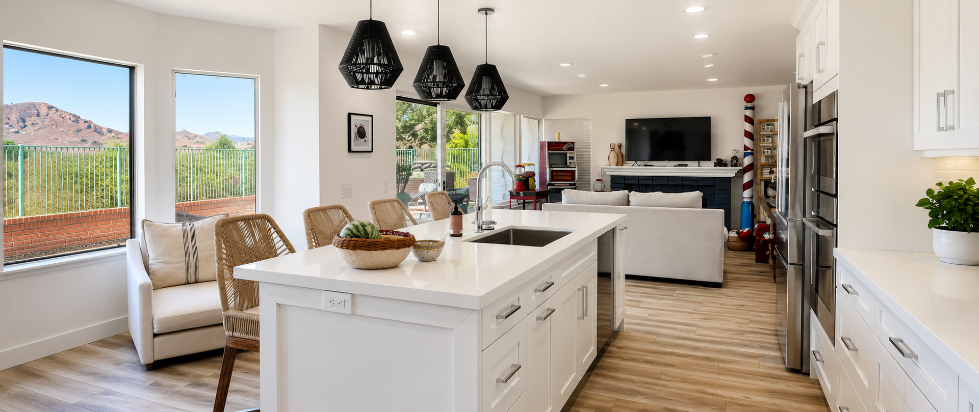 Bright modern kitchen with white island, black pendant lights, wood floors, and dining area by windows