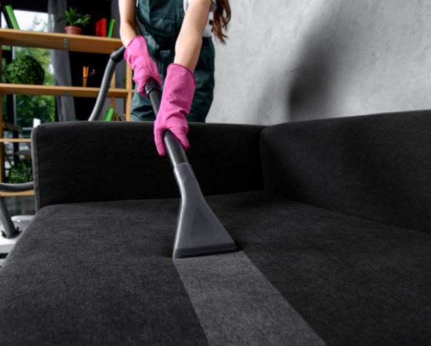 Person using a pink-gloved hand vacuuming a black sofa.
