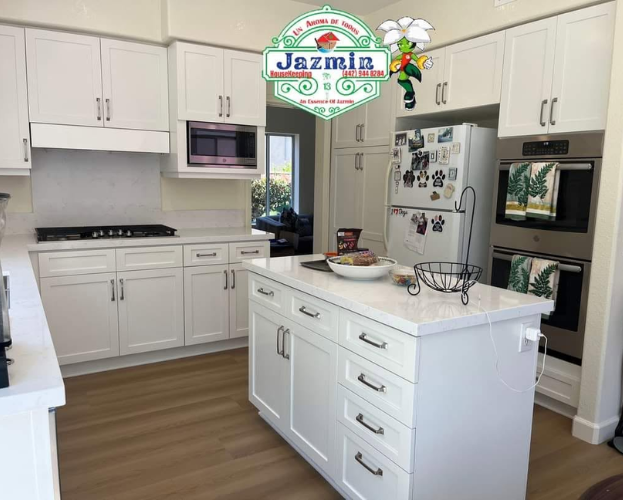 Bright white modern kitchen with island, built-in oven, stove, microwave, and refrigerator.